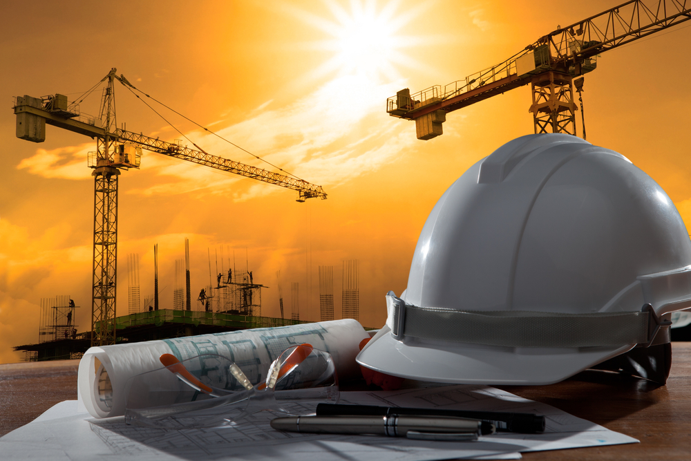 Safety helmet and architect pland on wood table with sunset scene and building construction